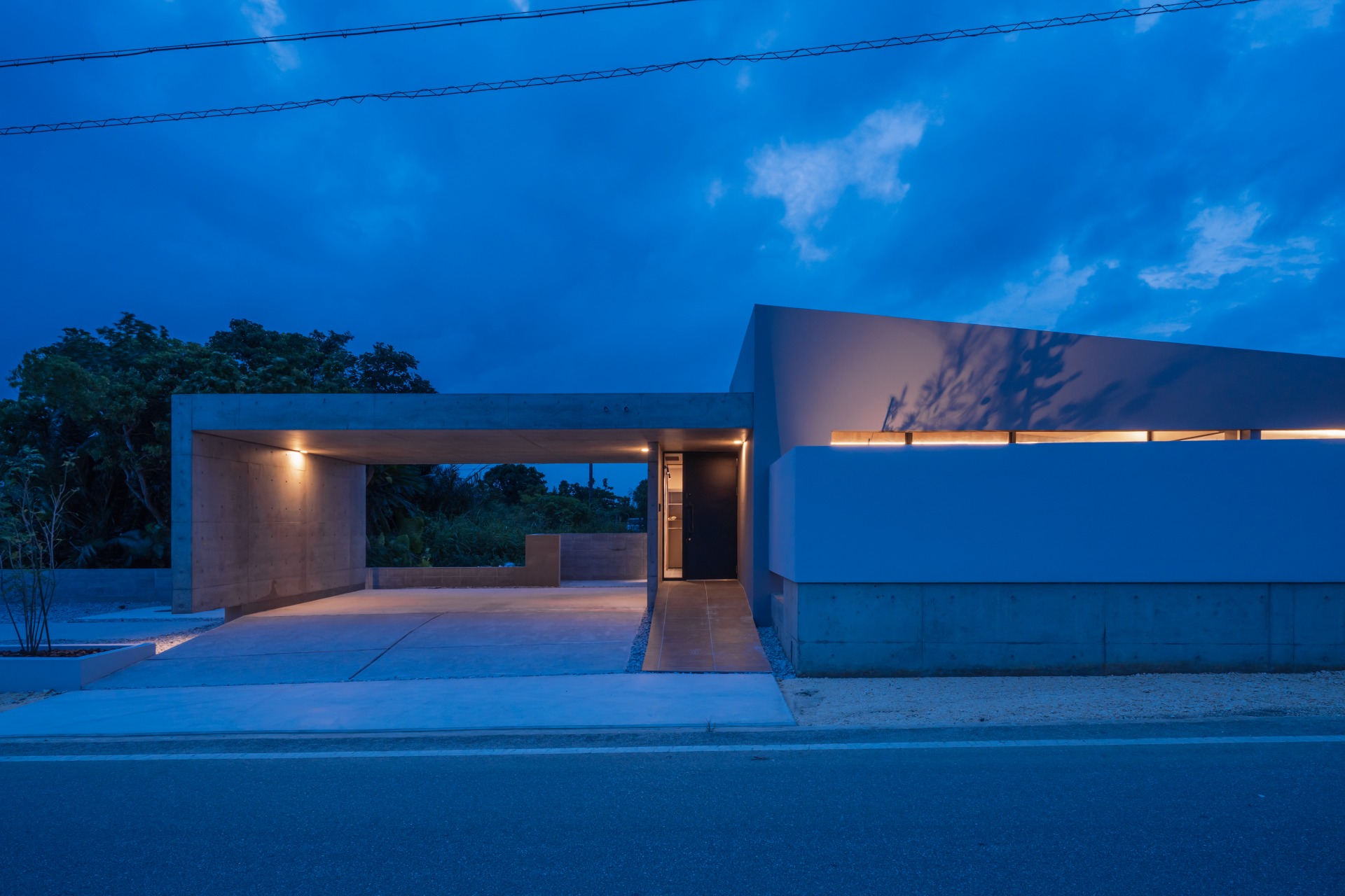 沖縄の細長い敷地に建つコンクリート平屋住宅の外観 テラスとつながる開放的なLDK空間 和室と一体となったモダンリビング 間接照明で演出された玄関空間