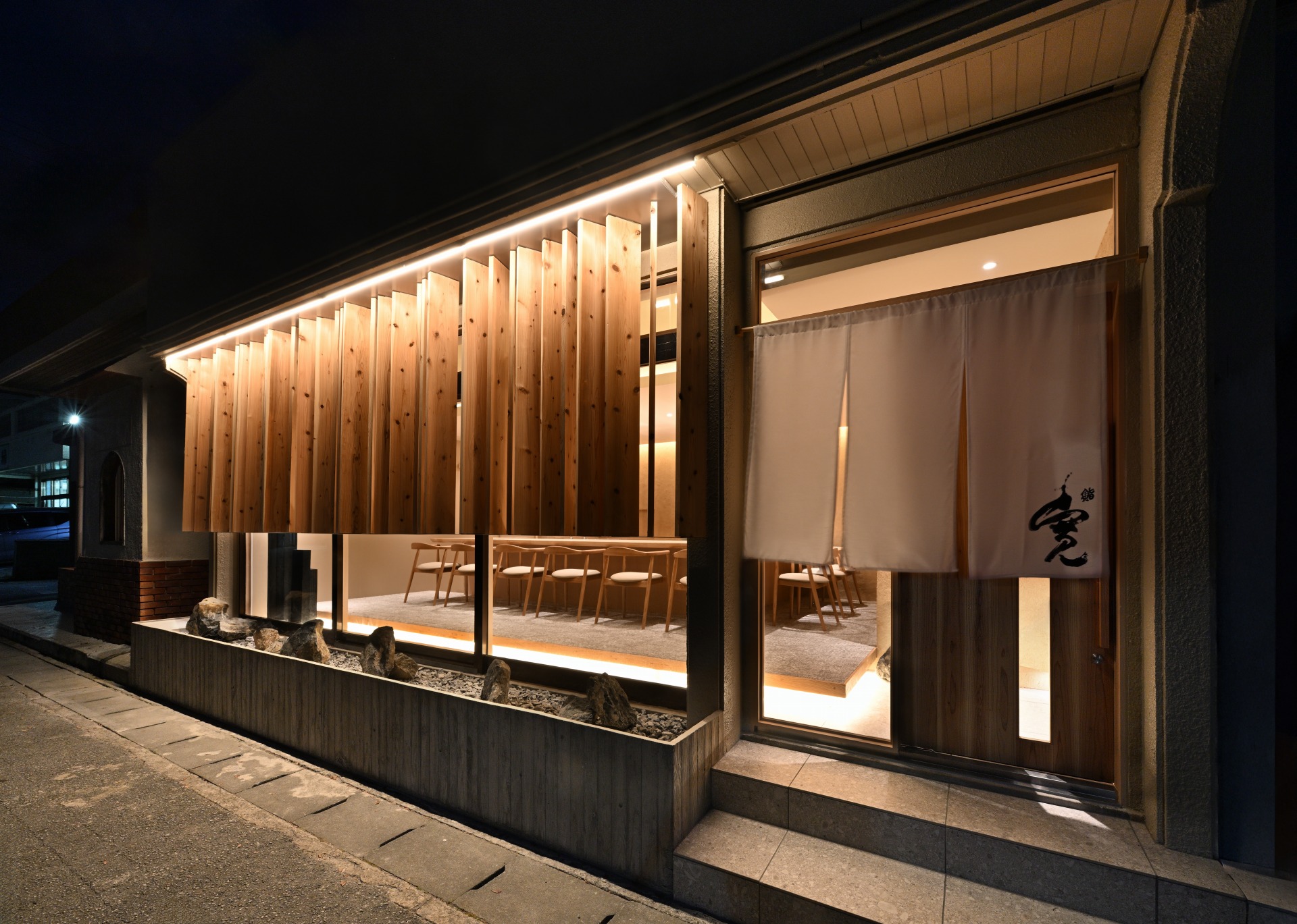 夜景時の寿司店ファサード。木製ルーバーと温かい照明が特徴の9席限定の寿司店